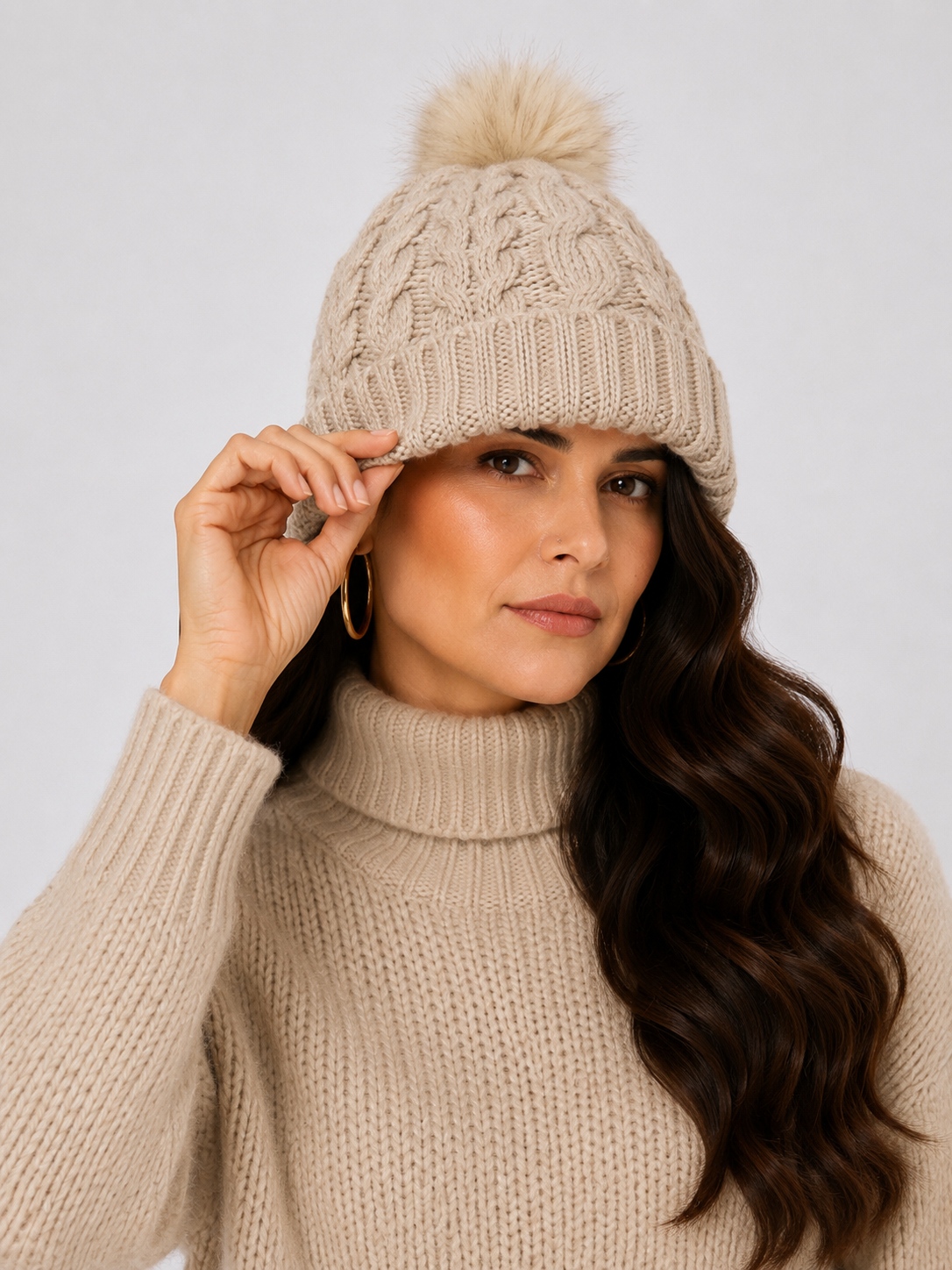 Mujer usando gorro tejido color marfil con diseño de trenzas y pompón de pelo sintético.